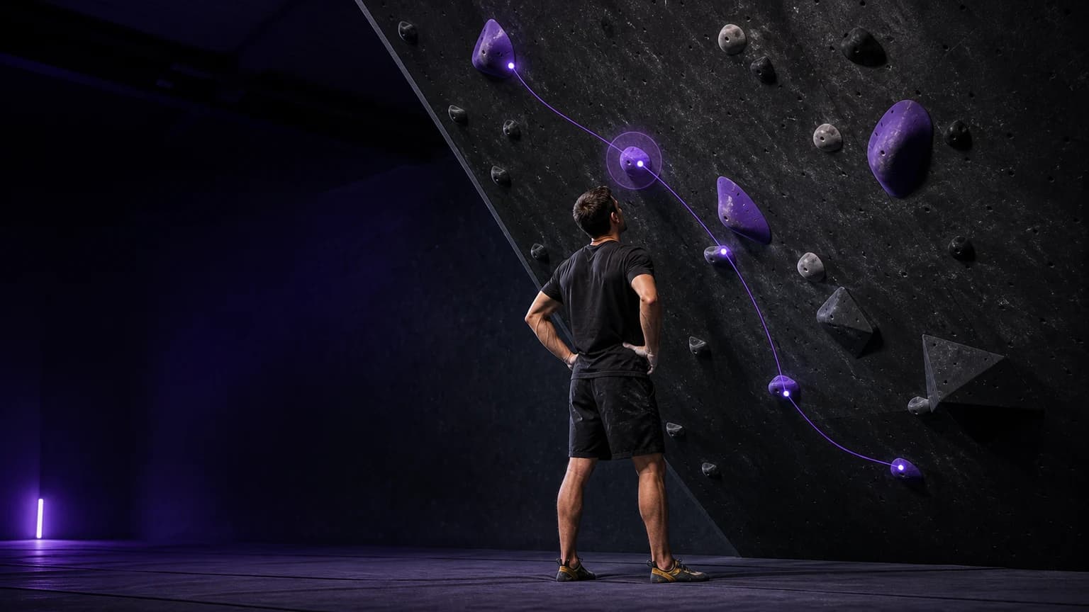 Climber studying a purple boulder sequence before another attempt in an indoor gym